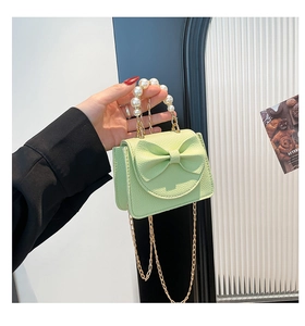 Detail of light green quilted mini bag with leather bow, pearl handle, and gold chain