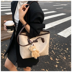 Close-up of beige tote bag with litchi texture and brown trim including a plush bear charm