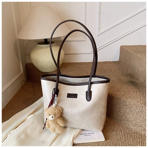 Detail of cream faux leather tote bag with dark brown handles and plush bear charm