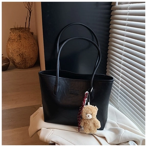 Detail of black faux leather tote bag with FASHION logo tag and plush bear charm