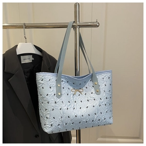 Détail du sac cabas plissé bleu clair avec imprimé nœud noir et décor de nœud doré