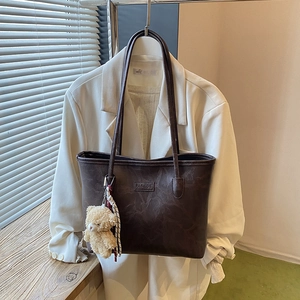 Deep brown leather tote bag with a plush bear charm hanging on a white blazer