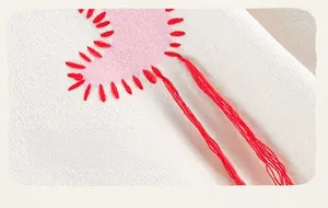Detail of pink heart patch with red hand-stitched embroidery and tassels on white sweatshirt