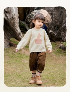 Detail van beige gebreide trui met konijntekening en bruine corduroy broek