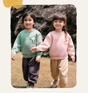 Detail of knit kids sweaters with contrast stitching and cuffed casual trousers in outdoor setting