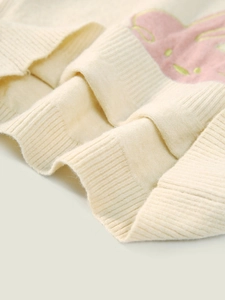 Gebreide kindertrui in crème met roze konijnpatroon en een geribbelde zoomdetail