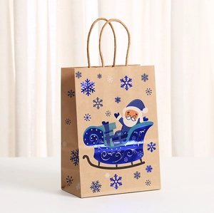 Blue foil Christmas kraft paper gift bag featuring Santa Claus and reindeer on a white table