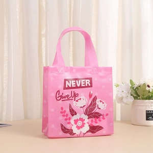 Sac cadeau rose en non-tissé avec motif floral et texte Never Give Up sur table