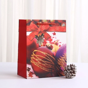 Christmas gift bag with festive red ornaments, gold glitter, and red woven handles