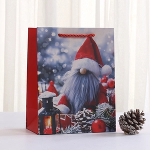 Sac cadeau de Noël en papier avec motif gnome, anses rouges et décor hivernal enneigé