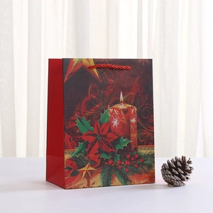 Christmas paper gift bag featuring poinsettia flowers and candles with red rope handles
