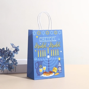 Hanukkah kraft gift bag with dreidel prints and white rope handles on beige surface