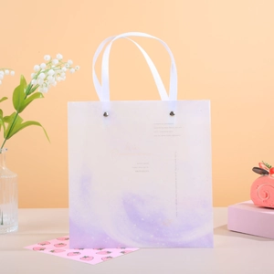 Detalle de bolsa de regalo degradada morada con asas de cinta y letras doradas de arte