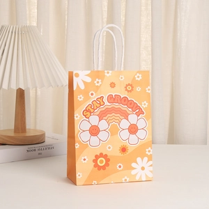 Floral print paper gift bag with 'Stay Groovy' text and white handles on a desk