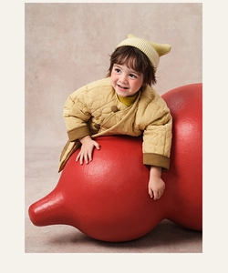 Quilted yellow jacket with traditional buttons on child leaning on red prop