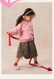 Close-up of pink crewneck sweatshirt with ruffle details and brown quilted skirt for girls