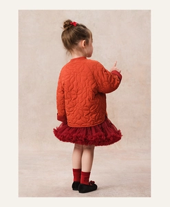 Rear view of girl in quilted orange jacket and dark red mesh skirt for winter festival