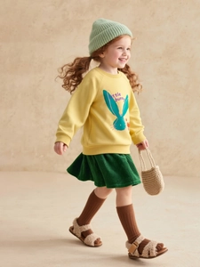 Girl's autumn outfit featuring yellow bunny sweatshirt and green corduroy pleated skirt