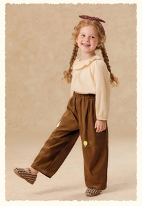 Detail of girls' corduroy trousers with delicate yellow flower embroidery on dark brown fabric
