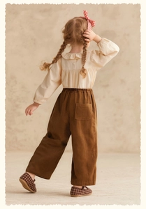 Back view of girl in beige ruffle shirt and brown corduroy pants for a stylish fit