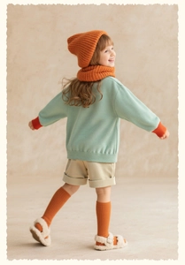 Detail of girls mint green sweatshirt with orange rib cuffs and khaki corduroy shorts