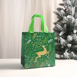 Close-up of green Christmas non-woven gift bag with golden reindeer and snowflake print