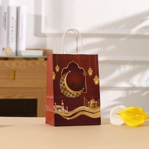 Dark red Ramadan gift bag with gold mosque print and moon motifs in a cozy setting