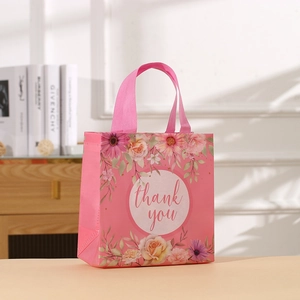Pink non-woven gift bag with floral patterns and Thank You text on a desk