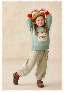 Detail of girl's green knit sweater with cupcake motif and khaki corduroy joggers