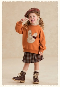 Detail of girls orange rabbit sweatshirt paired with plaid pleated skirt and beret