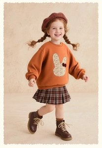 Detailed shot of an orange girls' rabbit sweatshirt and vintage plaid pleated skirt set