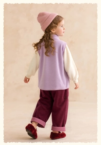Detail view of girl's purple fleece vest paired with red corduroy pants and pink knit hat