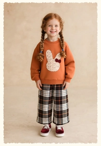 Detail of toddler girl wearing orange rabbit sweatshirt with floral patchwork and plaid pants