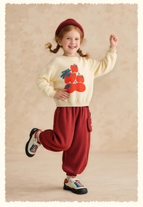 Full view of girl's beige apple sweatshirt and red corduroy pants with a knit hat
