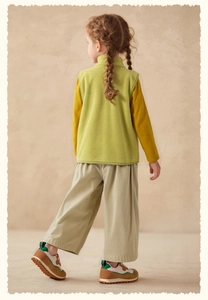 Back view of girl wearing green fleece vest with beige corduroy pants and sneakers