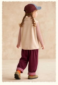 Back view of a girl in a beige fleece vest, striped shirt, and corduroy pants