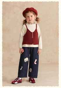 Detail of girls vintage school style outfit with burgundy vest and letter patch jeans