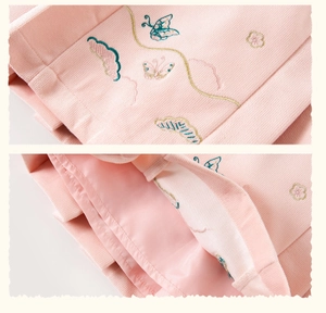 Détail de la broderie oiseaux et fleurs sur tissu texturé nid d'abeille rose