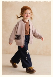 Close-up of children's beige knit cardigan with floral pockets and navy casual pants
