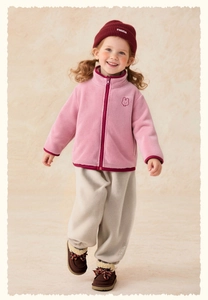 Ragazza in giacca in pile rosa con ricamo di coniglio, pantaloni beige e stivali da neve