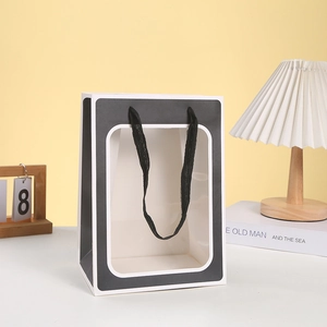 Detail of a paper gift bag with a large transparent window and black mesh handles