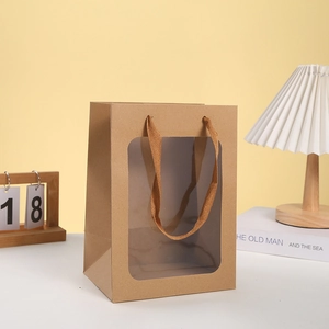 Kraft paper gift bag with large clear window and braided handles on white desk
