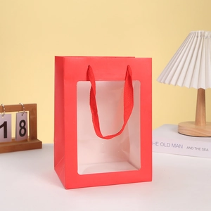 Detail of red gift paper bag with clear window and matching woven handle in cozy home setting