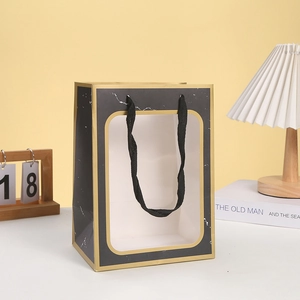 Detail of marble gift bag with transparent window, gold trim, and black woven handle