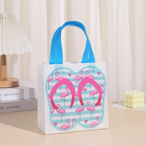 Close-up of white gift bag with blue handles featuring flamingo and flip-flop summer prints