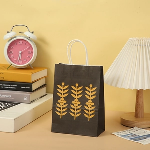 Detail of a black marble texture paper gift bag with yellow leaf prints and white handles