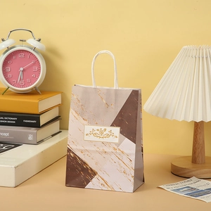 Detail of marble pattern gift bag with gold floral frame and woven handles in a cozy setting