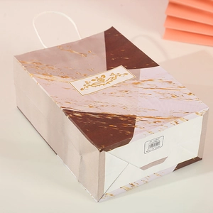 Detail of pink marble kraft paper gift bag with gold floral patterns and white handles