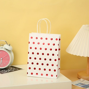 Detail of white kraft gift bag with red polka dots and twisted rope handle on a desk