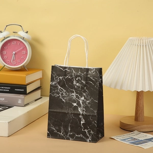 Elegant black marble pattern paper gift bag with white cotton rope handles in a home setting
